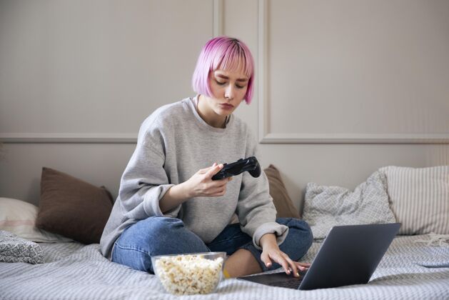 乐趣粉红色头发的女人在玩笔记本电脑上的操纵杆娱乐玩家技术