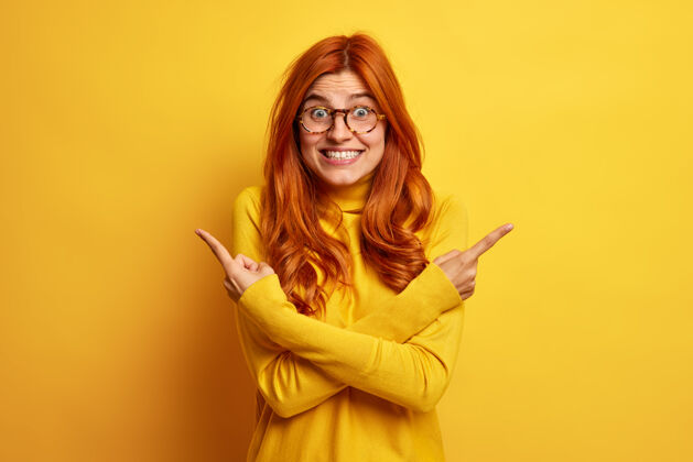 休闲正面红发的欧洲女人交叉手指 指向不同的侧面挑选两种不同的产品 穿着休闲的黄色高领毛衣站在室内有什么更好的选择美丽欢呼室内