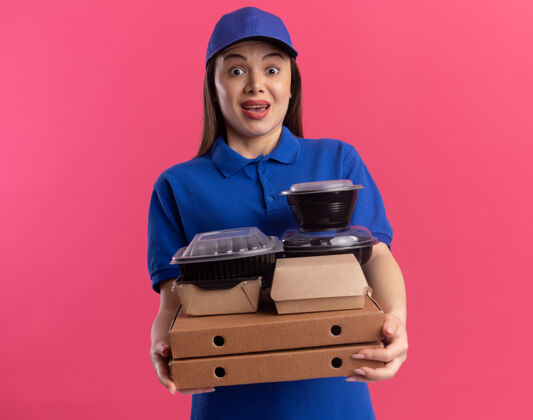 女人穿着制服的漂亮送货员拿着比萨饼盒上的食品包和容器 看着粉红色的相机漂亮食物粉色