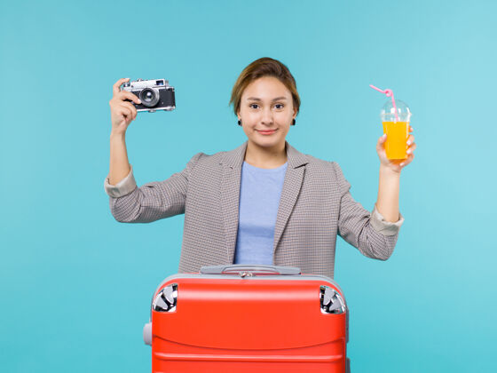 果汁前景度假中的女性手持新鲜果汁和相机在蓝色背景海上度假旅行微笑假期女人