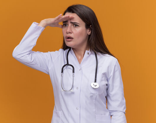 听诊器焦急的年轻女医生穿着带听诊器的医用长袍 手心不停地盯着额头看橙色的一边医疗女性焦虑