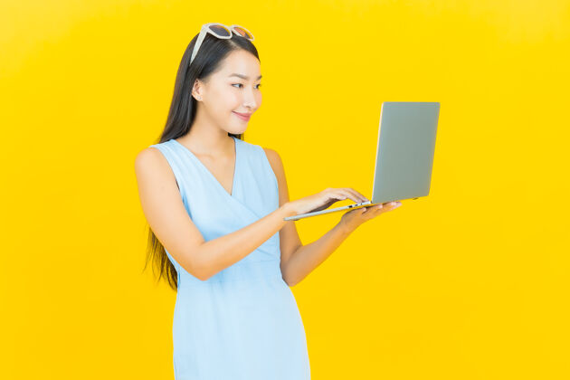 兴奋一幅美丽的亚洲年轻女子微笑的画像 黄色的隔离墙上挂着一台笔记本电脑成功脸企业家