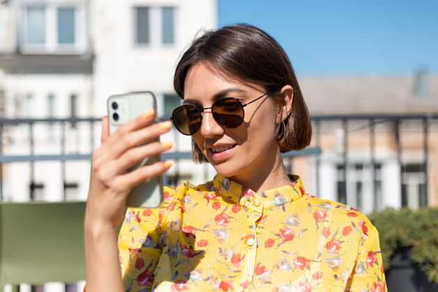 聊天阳光明媚的日子里 夏日咖啡馆露台上穿着黄色衣服的女人拿着手机成人互联网人
