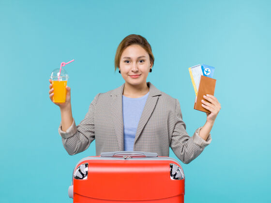 前面正面图：度假中的女性手持新鲜果汁和蓝色背景海上度假飞机的机票蓝色举行果汁