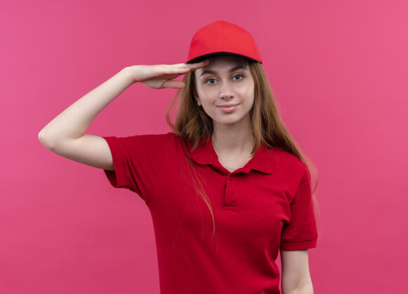 额头穿着红色制服的自信的年轻女送货员把手放在孤立的粉色空间靠近前额粉色红色交货