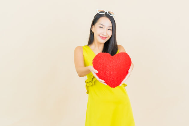 颜色肖像美丽的亚洲年轻女子微笑与心枕形状的彩色墙上微笑快乐韩国人