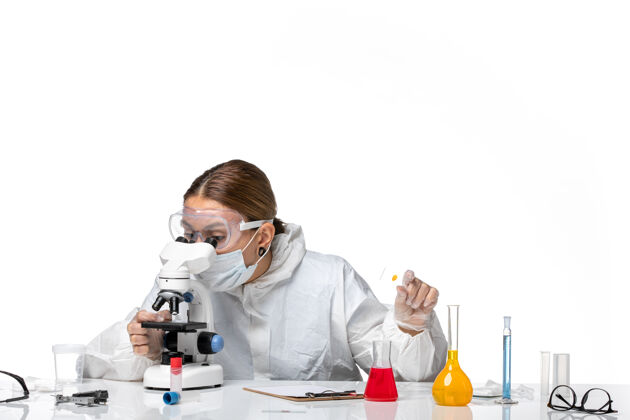 病毒正面图女医生穿着防护服 戴着口罩 用显微镜对着白色背景的医药卫生大流行病毒冠状病毒实验室健康白人