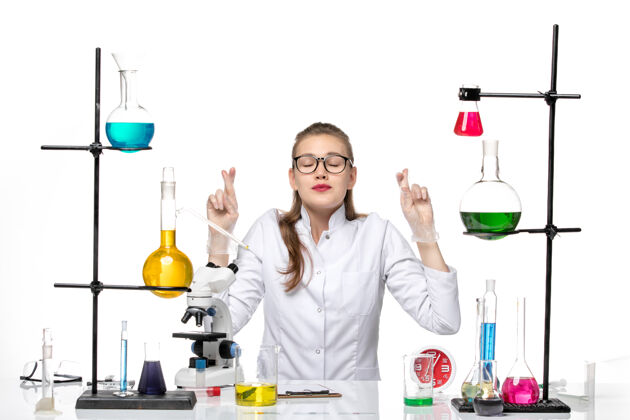 希望前视图穿着白色医疗服的女医生坐在桌子前 在白色背景上解决化学大流行坐玻璃化学