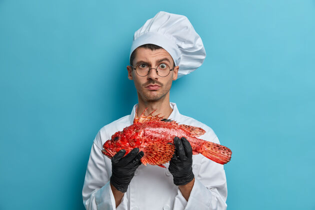 鱼严肃的男厨师端鱼的照片直视镜头请教厨师准备什么更好试着美味的食谱帽子男举行