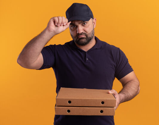 披萨自信的中年送货员穿着制服 戴着帽子 手里拿着披萨盒 手里拿着帽子 隔离在黄色的墙上中年自信男人