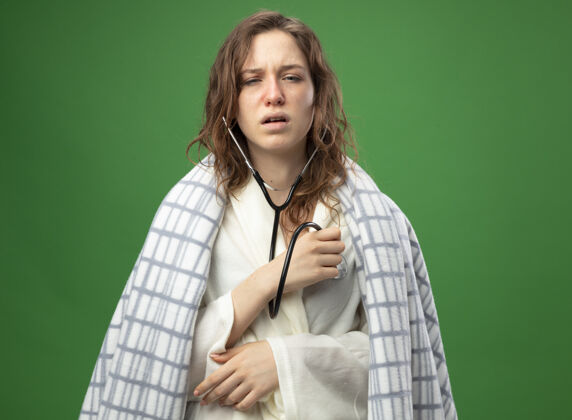 听诊器虚弱的年轻病女孩穿着格子布包裹的白色长袍 用绿色隔离的听诊器听自己的心跳穿年轻心跳