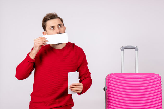 航班正面图：年轻男性 带着粉色包 手持白墙旅行票 彩色度假航班 夏季旅游者游客颜色微笑