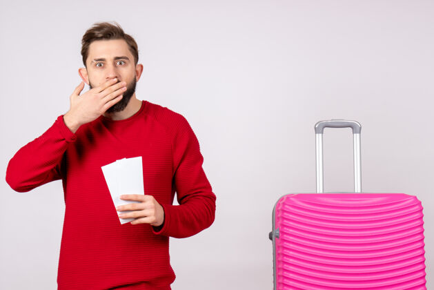 机票正面图：年轻男性 带着粉色包 手持白墙旅行的机票 彩色度假的机票 夏天的旅行年轻男性景观航班