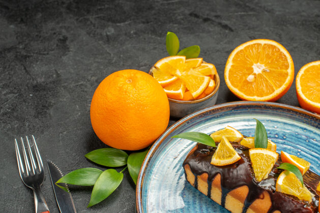 叉子横观黄色的柠檬和切好的蛋糕 用刀叉放在深色的桌子上刀子甜橙全切面