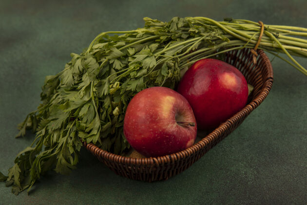 视野绿色背景下桶上新鲜的红色和甜苹果和欧芹的俯视图水果绿色苹果