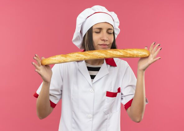 厨师身着厨师制服的年轻女厨师手捧着闻面包棒 眼睛紧闭 在粉色背景上与世隔绝拿着嗅眼睛