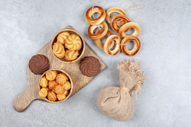 袋装在大理石背景的木板上 一个袋子和一个绑着苏什基的戒指紧挨着几碗饼干 棕色饼干紧挨着高质量的照片风味食欲饼干