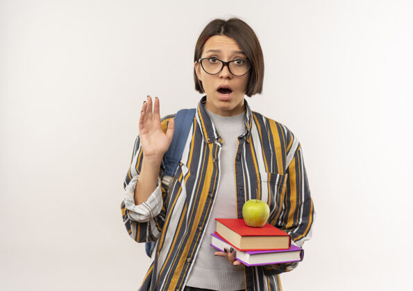 背印象深刻的年轻女学生戴着眼镜 背着书包 手里拿着苹果 手上举着白色的孤立物眼镜戴苹果