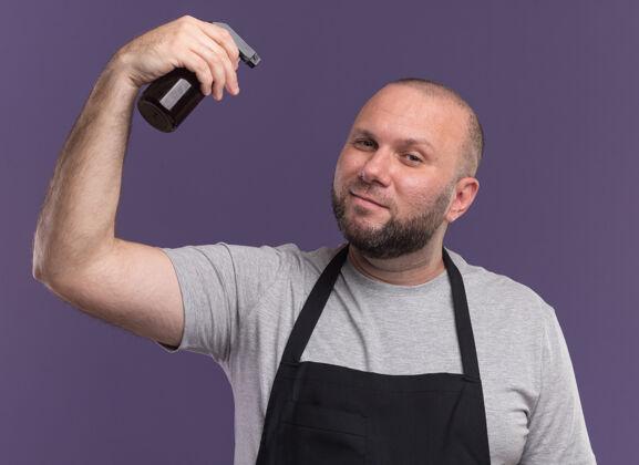 斯拉夫人高兴的斯拉夫中年男理发师在统一提高喷雾瓶隔离在紫色墙上喷雾瓶子请提高