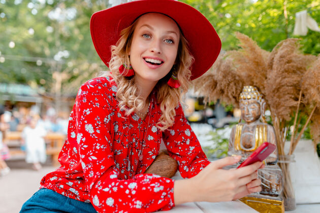 脸迷人的时尚金发微笑的女人在稻草红帽子和衬衫夏季时尚服装举行使用智能手机咖啡厅年轻金发女孩