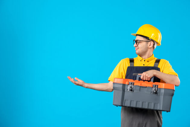制服蓝色墙壁上穿着制服 手拿工具箱的男建筑工人的正面图蓝色工人修理工