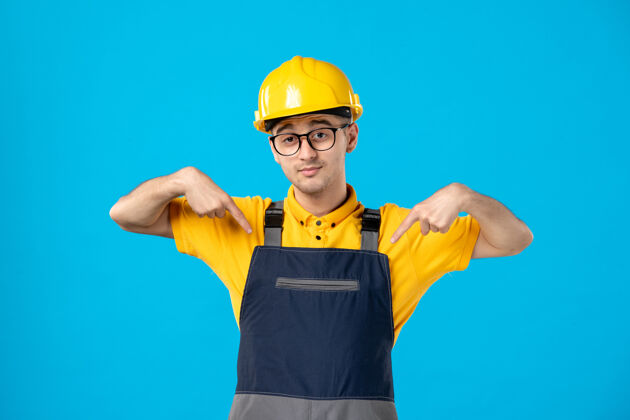 承包商蓝色墙壁上穿着制服和头盔的男建筑工人的正视图帽子建筑工人指点工