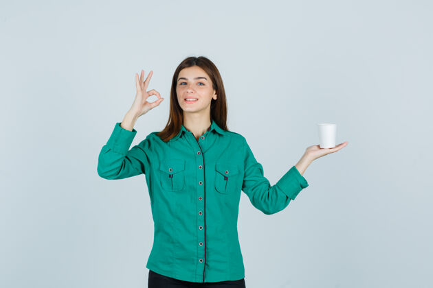 女人穿着衬衫的年轻女士手里拿着一杯塑料咖啡 一边摆着ok的姿势 看上去很开心 正对着窗外看漂亮手势微笑