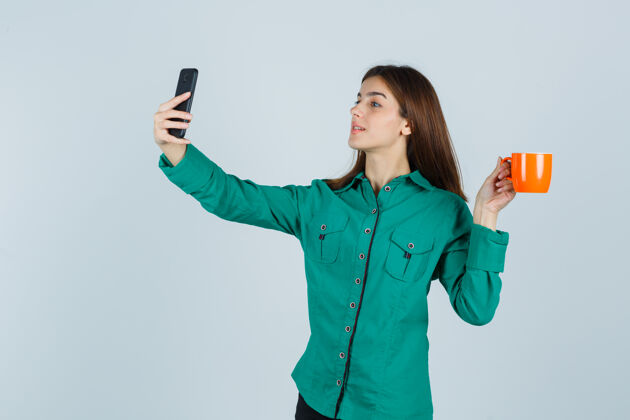 衬衫一位年轻的女士端着一杯橙黄色的茶 穿着衬衫拿着手机自拍 看上去很自信正面图肖像女人感性