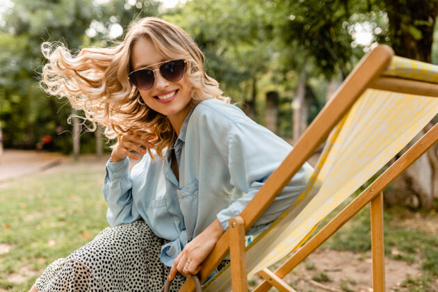时尚迷人的金发微笑的女人坐在躺椅上穿着夏天的衣服美丽积极衣服