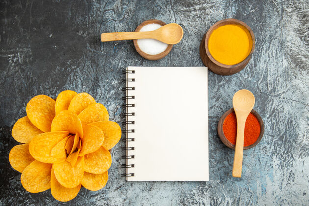 木勺上图：美味的薯片装饰成花朵形状的不同香料 上面放着勺子 灰色桌子上放着笔记本餐具花不同的