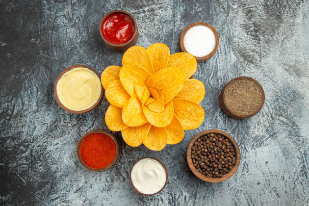 香料自制的土豆片装饰成花状 放在棕色的碗里 不同的香料和番茄酱蛋黄酱放在灰色的桌子上食物像自制