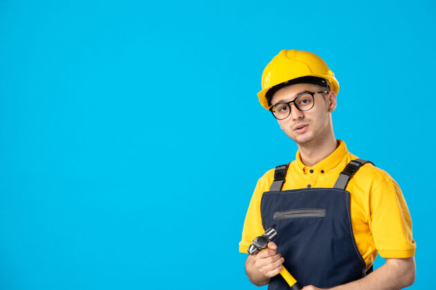 锤子蓝色墙壁上穿着制服手持锤子的男建筑工人的正视图视图工人勤杂工