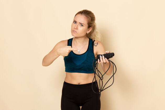 成人正面图身穿运动装的年轻女性手持跳绳在白墙上健康锻炼身体运动美容锻炼装备美女运动