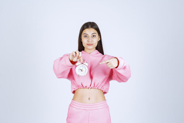 积极一个穿着粉色睡衣的女孩拿着一个闹钟 把它当作一个产品来推销人类人类服装