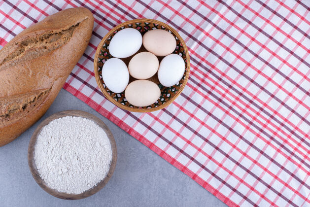 面团一篮子鸡蛋 一条面包和一碗面粉放在大理石表面碗面包桌布