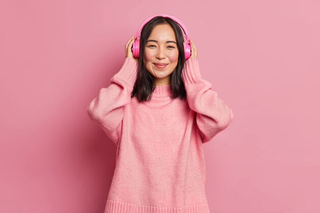 毛衣美丽的亚洲女性梅洛曼肖像戴无线电子立体声耳机听喜爱的音轨或流行歌曲用好听的音乐再现享受宁静的旋律穿粉色毛衣亚洲人跳投粉丝