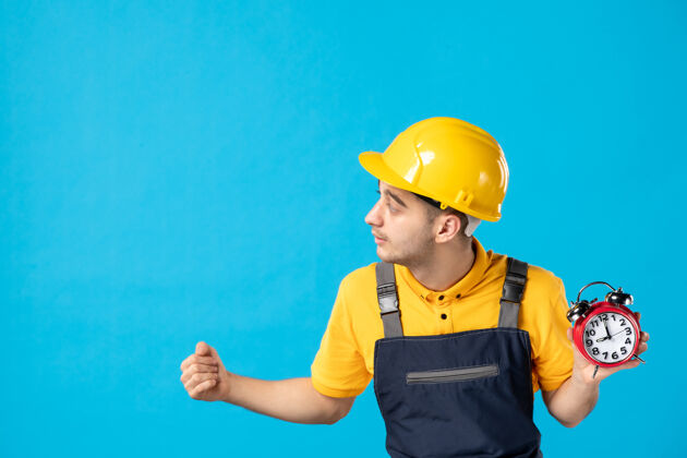 承包商身穿黄色制服 蓝色时钟的男性工人的正面图建筑师迟到头盔