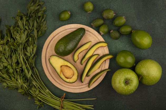 美食俯视图：绿色的鳄梨 切片放在木制的菜板上 刀子上夹着酸橙 青苹果 凤梨和欧芹 它们被隔离在绿色的表面上膳食健康切片