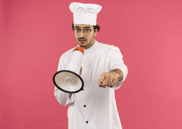 眼镜年轻的男厨师穿着厨师制服 戴着眼镜 用扩音器说话 向你们展示手势说话烹饪制服