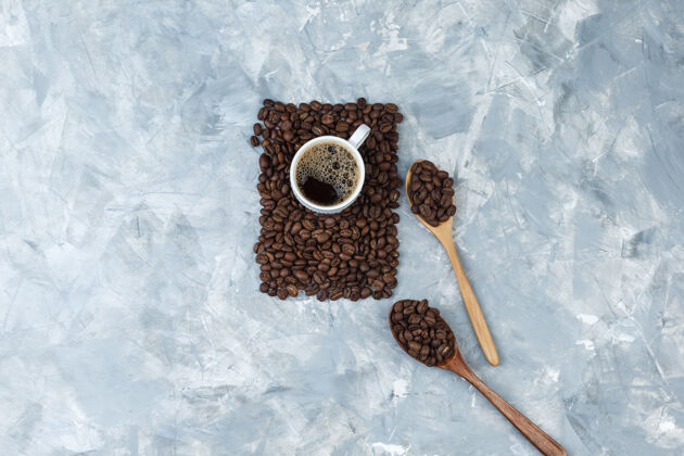 早晨一套咖啡和咖啡豆装在蓝色大理石背景上的木勺里顶视图卡布奇诺早餐质地