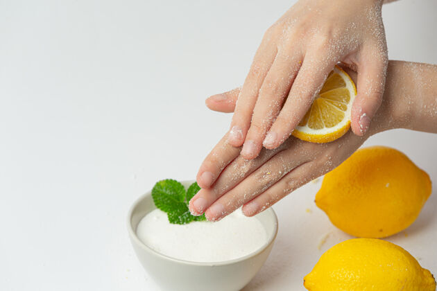 年轻年轻女子用天然柠檬磨砂膏擦手上的白色表面过程治疗护理