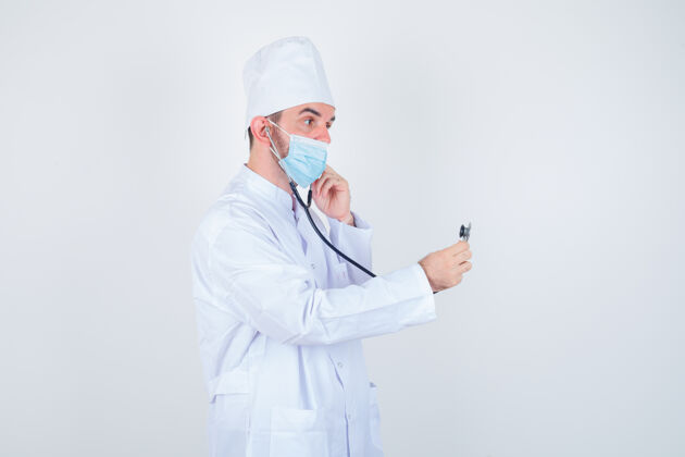实验室穿着白色医用实验服的帅哥 戴着口罩 耳朵里夹着听诊器的耳塞 好像他在听 看着很专注 前视图力量决心医疗