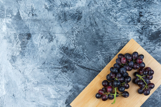 葡萄藤一些黑葡萄在粗糙的灰泥和砧板背景上 平放秋天叶子健康