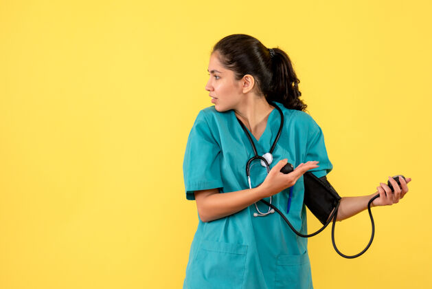 诊所正面图美丽的女医生穿着制服 用血压计站在黄色的背景上设备前面医学