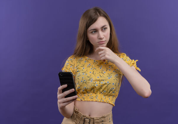 抱着一个体贴的年轻女孩拿着手机 手放在下巴上 隔着一堵紫色的墙 上面留着复印空间女孩手手机