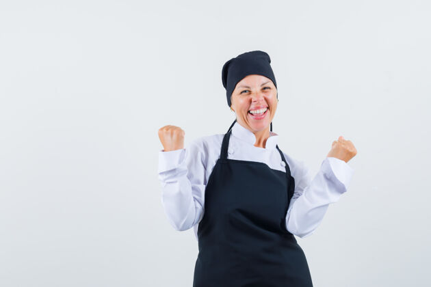 优雅身着制服的女厨师 围裙展示获胜者的姿态 看起来很幸福 正面视图优胜者肖像手