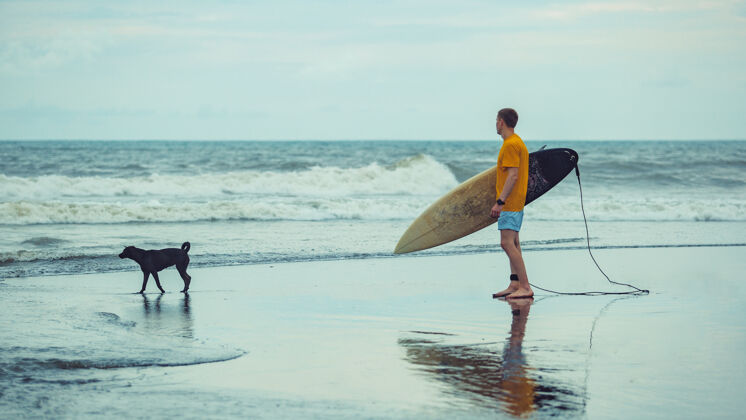 海洋一个男人拿着冲浪板站在海滩上海滩天堂冲浪者
