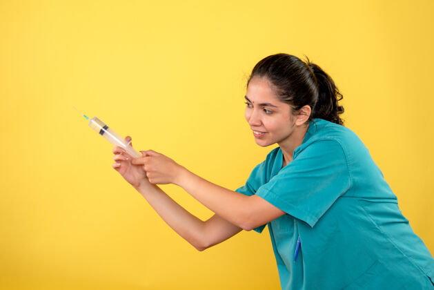 漂亮黄墙上年轻女医生使用注射器的正面图手持人年轻女医生