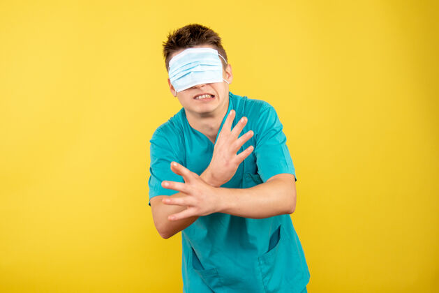 医院正面图：年轻的男医生 穿着医疗服 眼睛上戴着面罩 背景是黄色的医学健康病毒