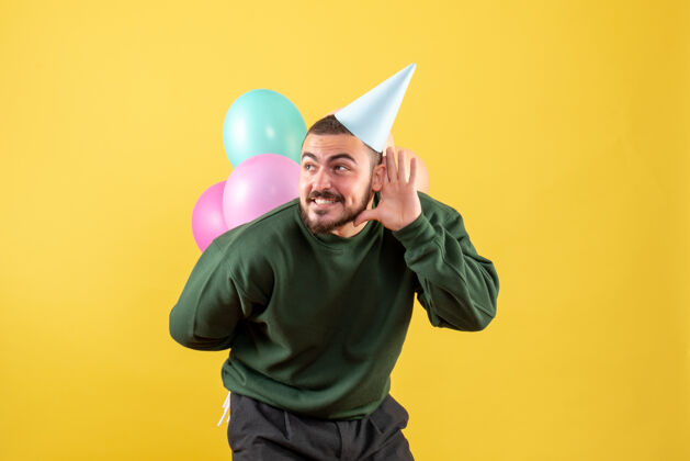 聚会正面图黄色背景上有彩色气球的年轻男性快乐帽子微笑